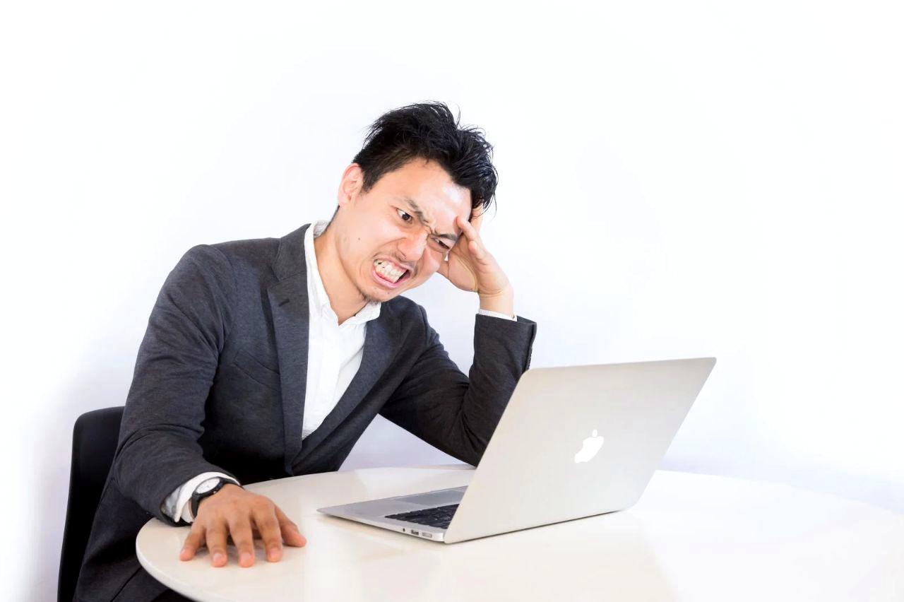パソコンに向かって悩むWebライターの男性。画面上に表示された3万円という数字が壁となっているイメージ